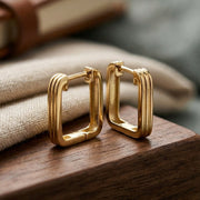 Gold hoop earrings on a wooden surface with a blurred background